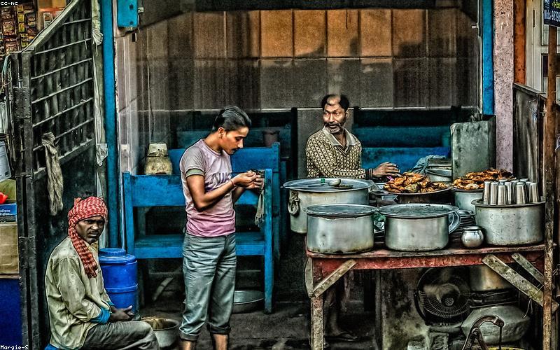 A group of friends animatedly discussing current affairs over cups of chai at a bustling street-side dhaba
