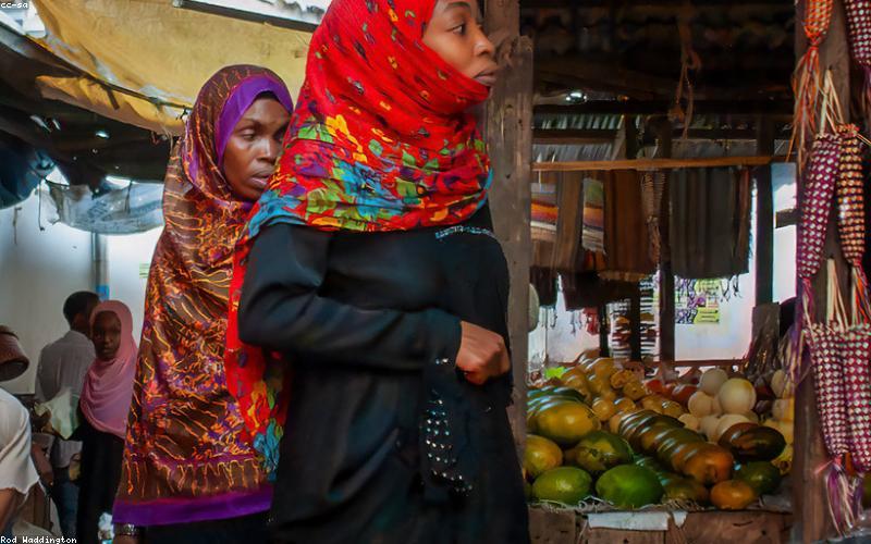 A happy group of young friends sharing a massive platter of loaded fries at a bustling food stall in a lively Pakistani market.